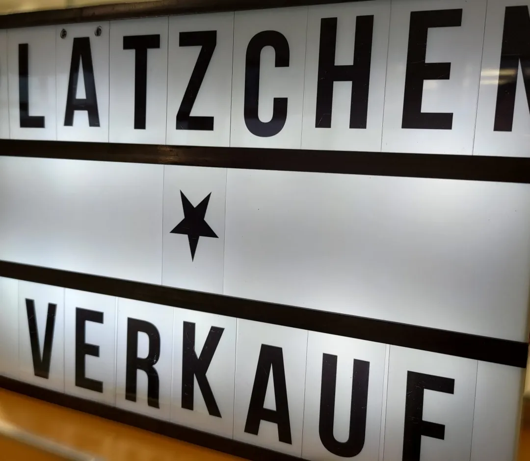 Lightbox auf einer Holzoberfläche. Die schwarzen Großbuchstaben auf der weißen Leuchtfläche bilden den Text PLÄTZCHEN VERKAUF, getrennt durch ein schwarzes Stern-Symbol in der Mitte.