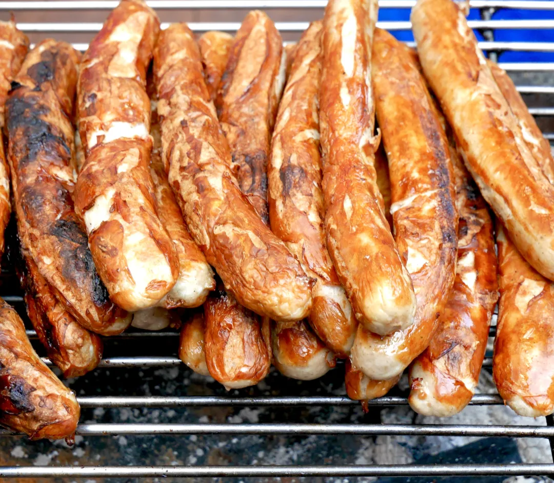 Nahaufnahme von gegrillten Würsten, die auf einem Grillrost gestapelt sind.