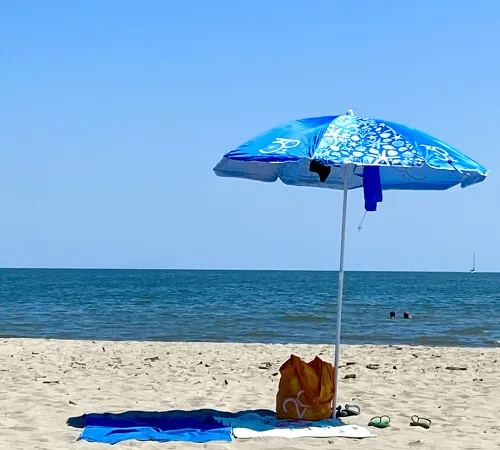 Sonnenschirm und Badehandtücher an einem Sandstrand vor blauem Meer