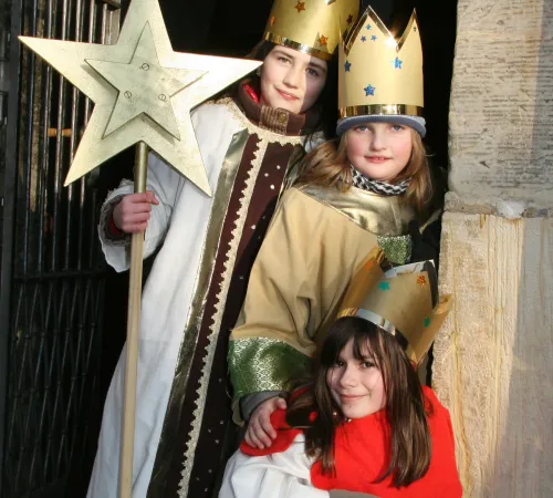 Drei Kinder als Sternsinger verkleidet, mit Kronen und Stern in der Hand.