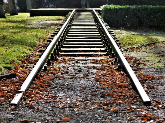 Altes Bahngeleise endet im Park, umgeben von Herbstlaub und grünem Rasen.