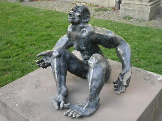 Expressionistische Bronzeskulptur einer sitzenden, nackten männlichen Figur mit deformierten Proportionen auf einem Steinsockel. Der Kopf ist weit in den Nacken geworfen, der Mund zum Schrei oder Gebet geöffnet, während eine Hand bittend geöffnet ist.
