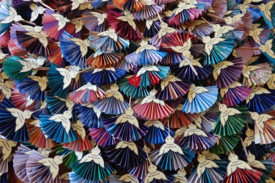 Gebastelte Taubenfiguren aus Papier. Auf dem hellgelben Körper des Vogels steht der Text "Gottes Windhauch", die Flügel sind als farbige Papierfächer gestaltet.