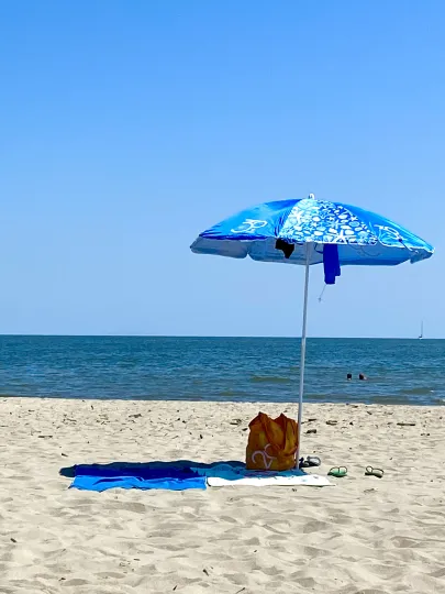 Sonnenschirm und Badehandtücher an einem Sandstrand vor blauem Meer