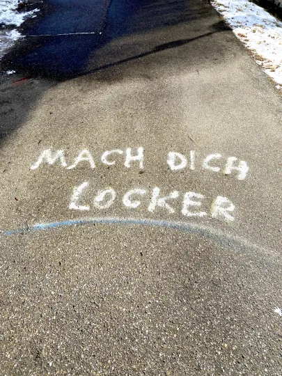 Mit weißer Kreide geschriebene Botschaft auf einer asphaltierten Fläche. Der Text lautet MACH DICH LOCKER.