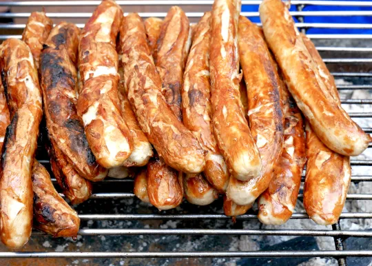 Nahaufnahme von gegrillten Würsten, die auf einem Grillrost gestapelt sind.