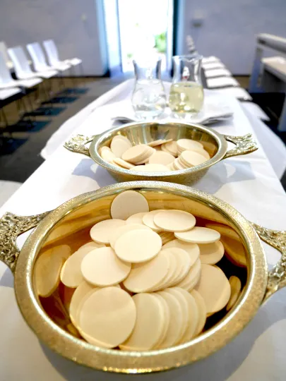 Hostienschalen stehen auf einem Kredenztisch bereit, im Bildhintergrund Glaskrüge mit Wasser und Wein.
