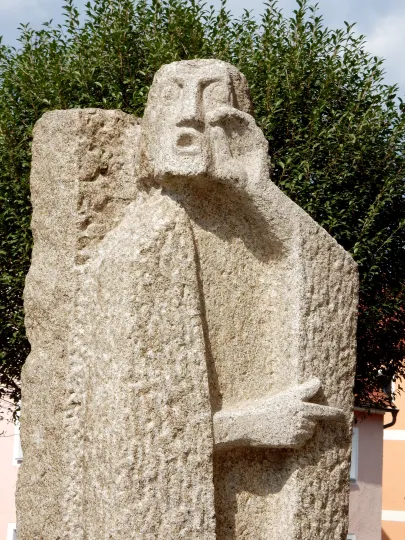 Moderne Granitskulptur von Johannes dem Täufer. Die abstrakte Figur zeigt ein Gesicht mit schreiendem Mund und eine Hand mit ausgestrecktem Zeigefinger, die in eine Richtung deutet.