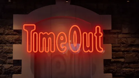 Rot leuchtender Schriftzug „TimeOut” vor einer Mauer