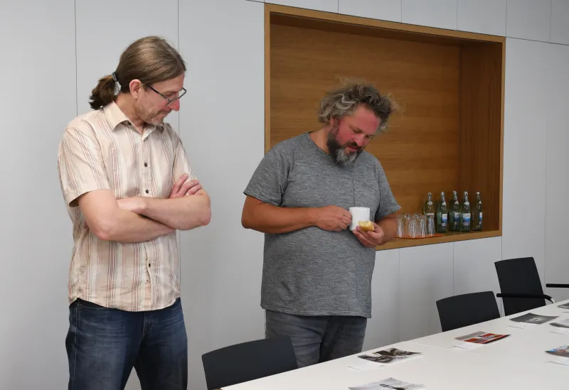 Zwei Männer betrachten Fotos auf einem Tisch in einem modernen Besprechungsraum.