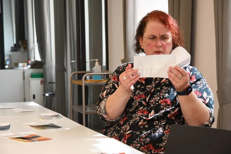 Frau mit roten Haaren betrachtet nachdenklich ein gefaltetes Papier am Tisch.